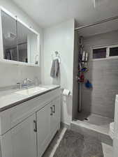 Bathroom featuring vanity, a tile shower, a textured ceiling, and light tile patterned floors