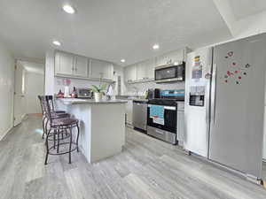 Kitchen with appliances with stainless steel finishes, a kitchen bar, a textured ceiling, a peninsula, and light stone countertops