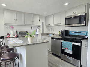 Kitchen featuring stainless steel appliances, a kitchen bar, a textured ceiling, light stone counters, and a peninsula