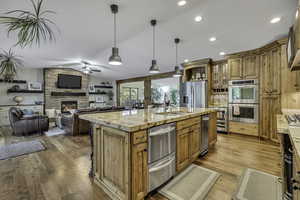 Kitchen featuring pendant lighting, light stone countertops, glass insert cabinets, lofted ceiling, and stainless steel appliances