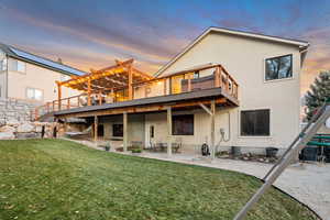 Back of house at dusk featuring a patio area, a lawn, stucco siding, and a pergola