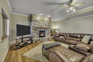 Living area with light wood-type flooring, a stone fireplace, a ceiling fan, and crown molding