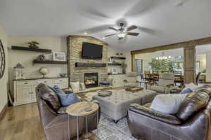 Living room with ceiling fan, lofted ceiling, light wood-type flooring, a chandelier, and a stone fireplace