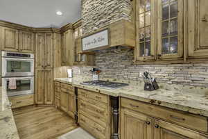 Kitchen featuring appliances with stainless steel finishes, light wood finished floors, glass insert cabinets, custom range hood, and light stone counters