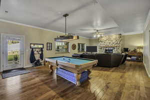Rec room with crown molding, hardwood / wood-style floors, pool table, a stone fireplace, and ceiling fan