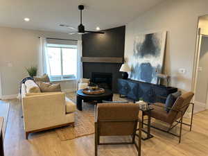 Living area with a large fireplace, lofted ceiling, recessed lighting, light wood-type flooring, and ceiling fan