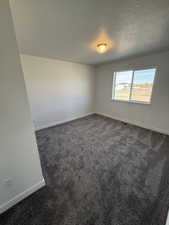 Empty room featuring dark carpet and a textured ceiling
