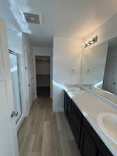 Bathroom featuring a walk in closet, double vanity, light wood-style floors, a textured ceiling, and a stall shower