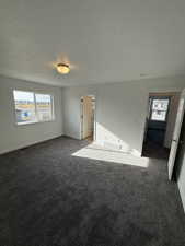 Owners bedroom featuring healthy amount of natural light, dark colored carpet, and a textured ceiling