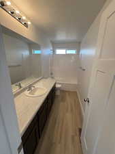 Bathroom featuring vanity, shower / bathtub combination, light wood-style floors, and a textured ceiling