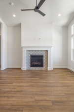Unfurnished living room with a tiled fireplace, ceiling fan, wood finished floors, and recessed lighting