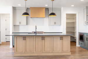 Kitchen with backsplash, light wood-type flooring, stainless steel microwave, a center island with sink, and recessed lighting