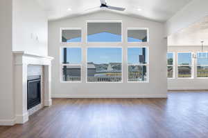 Unfurnished living room with dark wood-style floors, a tiled fireplace, ceiling fan, a chandelier, and high vaulted ceiling