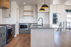 Kitchen with stainless steel appliances, a center island with sink, gray cabinetry, pendant lighting, and recessed lighting