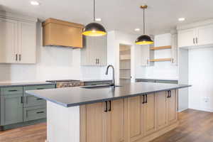 Kitchen with decorative backsplash, dark wood finished floors, hanging light fixtures, an island with sink, and recessed lighting