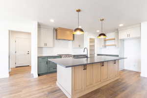 Kitchen featuring pendant lighting, a center island with sink, light wood-type flooring, white cabinets, and recessed lighting