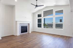 Unfurnished living room featuring a fireplace, dark wood-style floors, a ceiling fan, and high vaulted ceiling