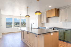 Kitchen featuring tasteful backsplash, a textured ceiling, a center island with sink, light wood finished floors, and pendant lighting