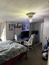 Bedroom with a textured ceiling, carpet floors, and an office area