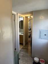 Hall featuring a textured ceiling, light wood-type flooring, and electric panel