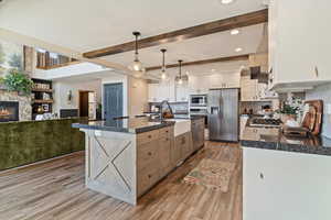 Kitchen featuring appliances with stainless steel finishes, open floor plan, decorative light fixtures, light wood finished floors, and a fireplace