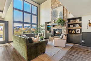 Living room featuring wood finished floors, a stone fireplace, built in shelves, and a towering ceiling
