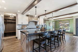 Kitchen with beam ceiling, hanging light fixtures, a kitchen bar, a kitchen island with sink, and white cabinets