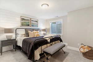 Bedroom with light colored carpet and wood walls