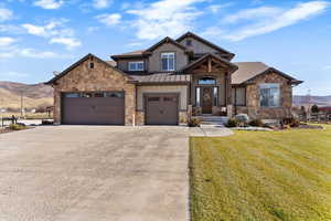 Craftsman house featuring a front lawn, driveway, stone siding, a metal roof, and a standing seam roof
