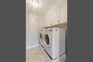 Laundry room featuring washer and dryer, wood finish floors, cabinet space, and a chandelier