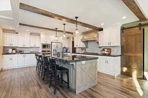 Kitchen featuring a barn door, beam ceiling, tasteful backsplash, a center island with sink, and pendant lighting