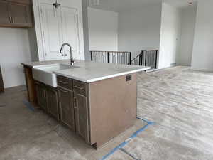 Kitchen with dark brown cabinetry, an island with sink, light stone counters, decorative light fixtures, and open floor plan