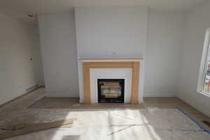Unfurnished living room featuring a glass covered fireplace and baseboards