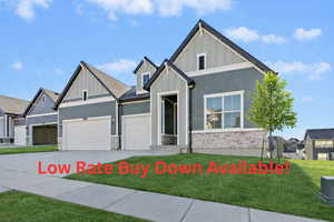 View of front of property with board and batten siding, stone siding, a front yard, concrete driveway, and a garage