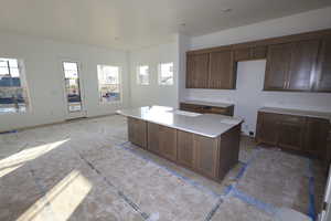 Kitchen featuring a center island, dark brown cabinets, and light stone counters