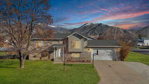 View of front facade with a lawn, concrete driveway, a mountain view, a shingled roof, and a garage