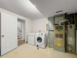 Laundry area featuring light floors, water heater, washer and dryer, a textured ceiling, and heating unit