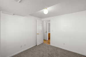 Carpeted empty room featuring a textured ceiling and baseboards