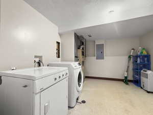 Laundry room with light floors, independent washer and dryer, electric panel, and a textured ceiling