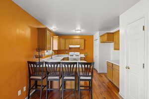 Kitchen with a kitchen bar, light countertops, white gas range, a peninsula, and dark wood finished floors