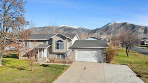 Split foyer home featuring a front yard, a mountain view, concrete driveway, roof with shingles, and an attached garage