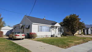 Bungalow with a front yard, roof with shingles, and an outbuilding