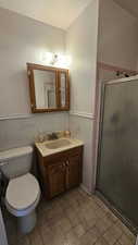Bathroom featuring vanity, a stall shower, wainscoting, and tile walls