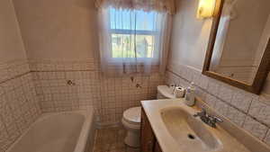 Full Bathroom with a garden tub, vanity, wainscoting, and tile walls