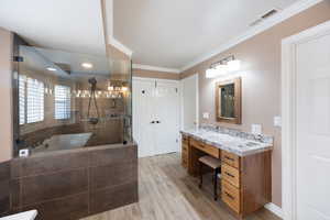 Full bathroom with a shower stall, light wood finished floors, vanity, a relaxing tiled tub, and ornamental molding