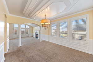 Unfurnished living room featuring a decorative wall, arched walkways, crown molding, a wainscoted wall, and decorative columns