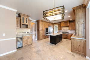 Kitchen with arched walkways, tasteful backsplash, light stone countertops, decorative light fixtures, and crown molding