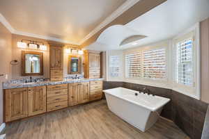 Full bath with double vanity, a soaking tub, ornamental molding, light wood-type flooring, and tile walls