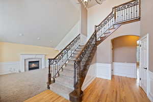 Stairway with wainscoting, a decorative wall, arched walkways, a glass covered fireplace, and wood finished floors