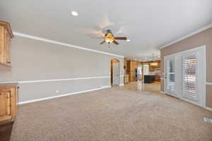 Unfurnished living room with light carpet, arched walkways, crown molding, recessed lighting, and ceiling fan
